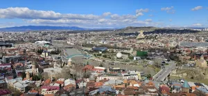 Una vista panorámica de Tbilisi, Georgia, con sus edificios históricos y modernos, tomada desde la cima de la Fortaleza de Narikala, destacando la diversidad arquitectónica y la rica herencia cultural del país.