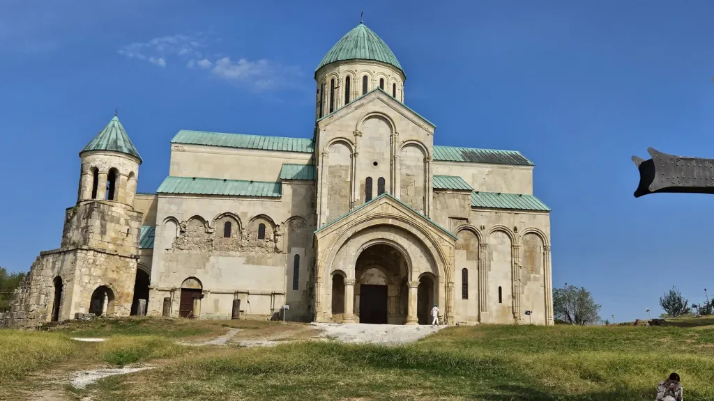 Vista panorámica de la Catedral de Bagrati, restaurada, con sus majestuosas cúpulas y piedra brillante al atardecer, reflejando la rica historia y arquitectura georgiana.
