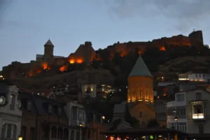 Vista da Praça Gorgasali para a imponente Catedral de São Jorge com a Fortaleza de Narikala ao fundo, destacando a riqueza histórica e arquitetônica de Tbilisi, a capital da Geórgia.