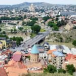 Vista panorámica de Tiflis al atardecer con el río Kurá, el Puente de la Paz iluminado y el casco antiguo de fondo