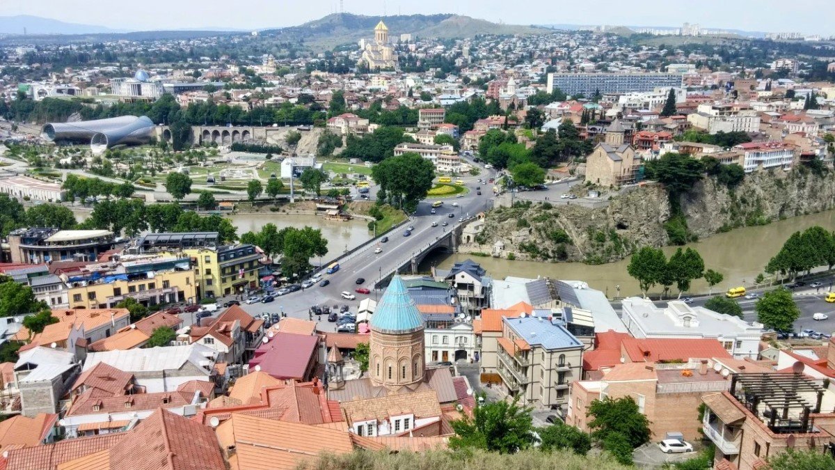 Vista panorámica de Tiflis al atardecer con el río Kurá, el Puente de la Paz iluminado y el casco antiguo de fondo